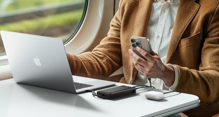 Mann lädt Laptop und Smartphone unterwegs mit Anker Laptop-Ladegerät.
